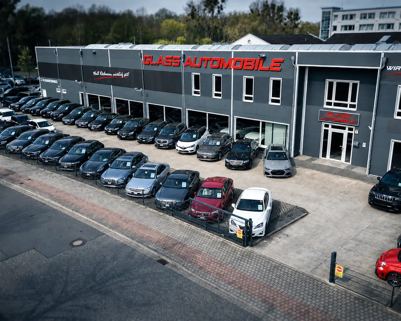 Vogelperspektive auf das Autohaus Glass Automobile mit einer großen Auswahl an Gebrauchtwagen und Premiumfahrzeugen auf dem Außenplatz.